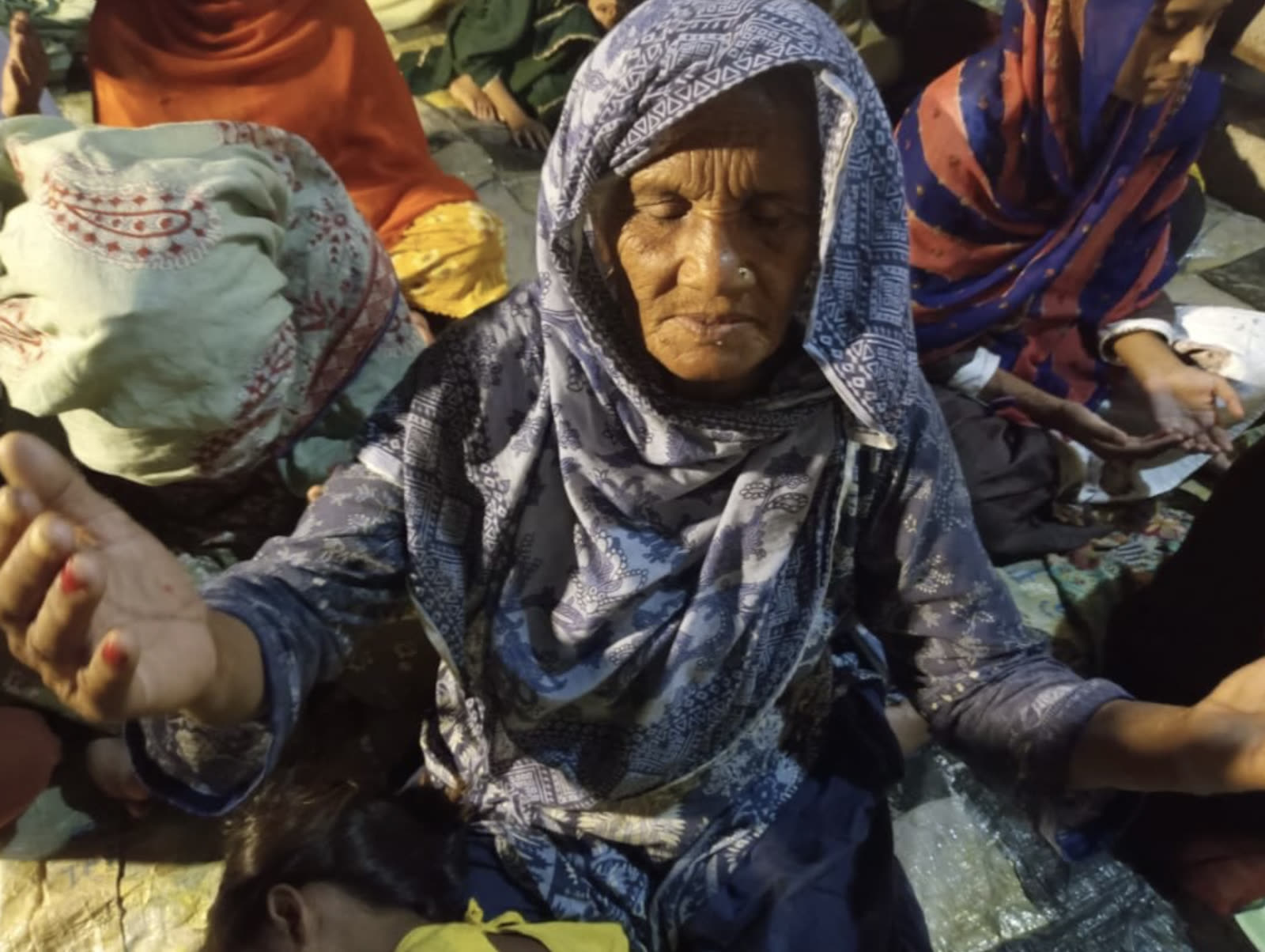 An older woman praying with open hands among a gathering